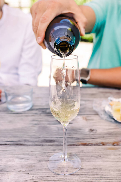 Close-up of man's hand pouring sparkling wine or champagne into the glass. Summer party - 写真・画像