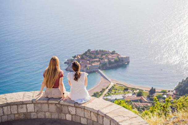 Two Woman tourist on background of beautiful view of the island of St. Stephen, Sveti Stefan on the Budva Riviera, Budva, Montenegro. Travel to Montenegro concept. - Photo, image