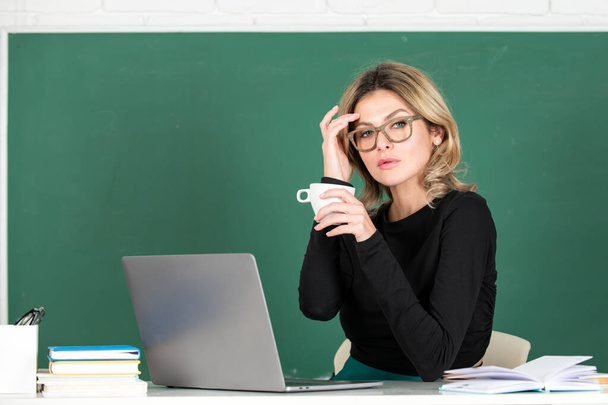 Young teacher or female student drinking coffee with notebook on a blank chalkboard - Foto, Bild