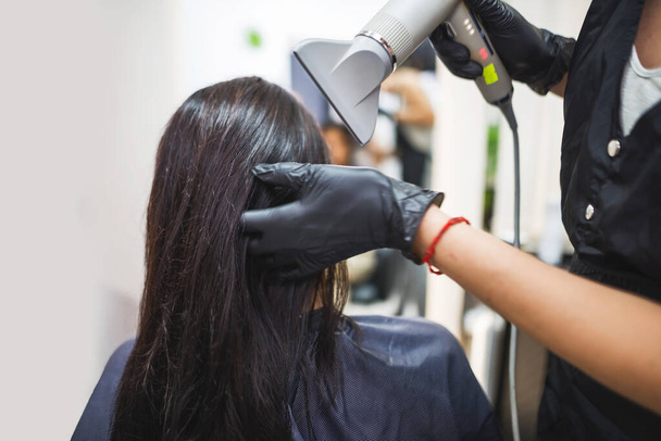 Drying long dark hair with a hairdryer.professional hairdresser dries the hair of a client in the salon, hairstyle beauty hair care, fashion service. - Fotoğraf, Görsel
