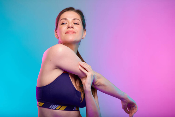 Sporty woman stretches arm muscles looking over shoulder. Female fitness portrait isolated on neon multicolor background. - Φωτογραφία, εικόνα