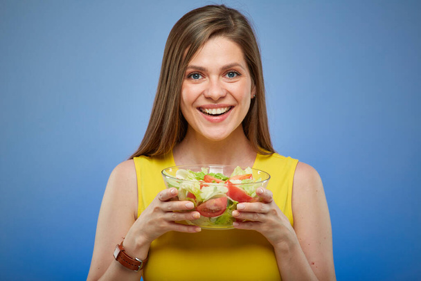 Smiling young lady in yellow dress holding glass bowl with salad. isolated female portrait. - 写真・画像
