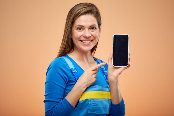 Woman in blue overalls holding smartphone and pointing finger at screen. Isolated female  worker portrait. - Foto, immagini