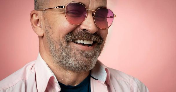 Portrait of a successful handsome smiling mature man in rose glasses on pink background. Close up of handsome beard man face with big white smile - Photo, Image