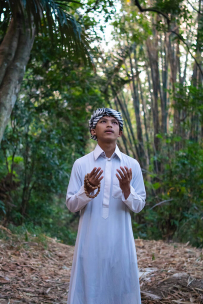 Arabský muž modlí v lese, zatímco na sobě bílé šaty s vážnou tváří v dopoledních hodinách - Fotografie, Obrázek