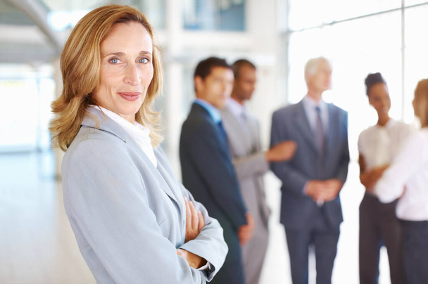 Confident female executive with business people conversing. Portrait of confident mature business woman with team conversing in background - Photo, image