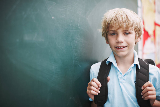 First one in class. Portrait of a young boy wearing a backpack and standing alongside copyspace at the blackboard - Fotoğraf, Görsel