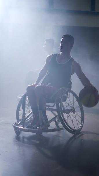 Mozgássérült sportoló kerekesszékes edzésen, kosárlabdával, drámai világítással. Függőleges videó - Felvétel, videó