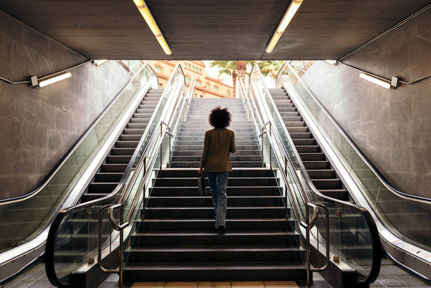 vista trasera de la silueta de una mujer de negocios irreconocible subiendo las escaleras de la estación de metro con un maletín en la mano, concepto de estilo de vida urbano y crecimiento - Foto, imagen