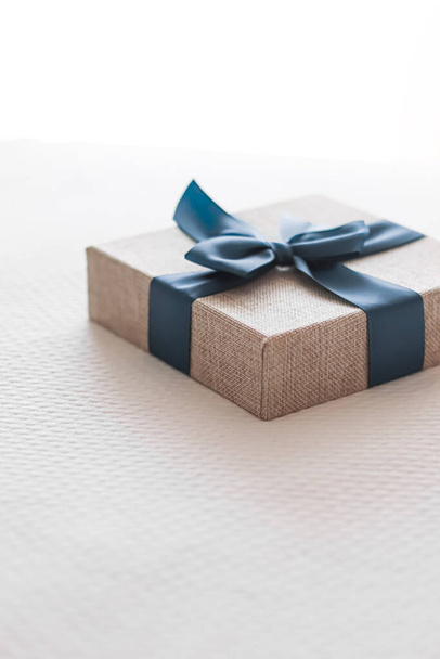 Holiday present and luxury online shopping delivery, wrapped linen gift box with blue ribbon on bed in bedroom, chic countryside style, close-up - Foto, afbeelding