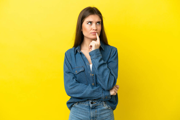 Young caucasian woman isolated on yellow background having doubts while looking up - Photo, Image