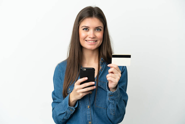 Νεαρή καυκάσια γυναίκα απομονωμένη σε λευκό φόντο αγοράζει με το κινητό με πιστωτική κάρτα - Φωτογραφία, εικόνα