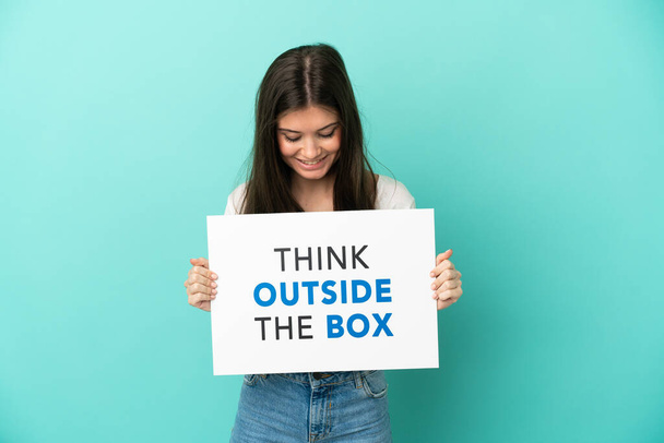Nuori valkoihoinen nainen sinisellä taustalla pitäen kylttiä, jossa teksti Ajattele laatikon ulkopuolella - Valokuva, kuva