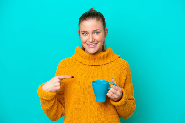 Молода біла жінка тримає чашку ізольовано на синьому фоні з несподіваним виразом обличчя
 - Фото, зображення