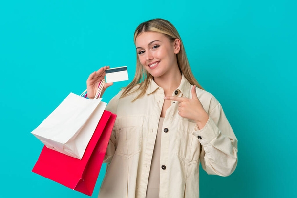 Junge Kaukasierin isoliert auf blauem Hintergrund mit Einkaufstaschen und Kreditkarte - Foto, Bild