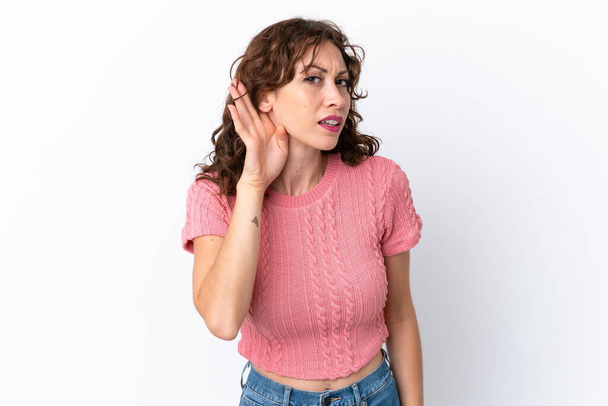 Молодая женщина с кудрявыми волосами изолированы на белом фоне слушать что-то, положив руку на ухо - Фото, изображение