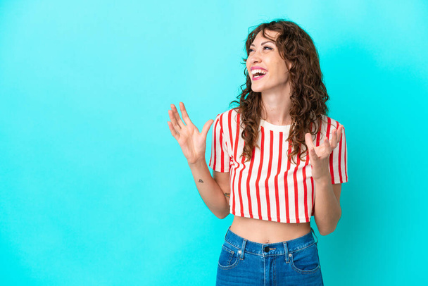 Young woman with curly hair isolated on blue background with surprise facial expression - Фото, изображение