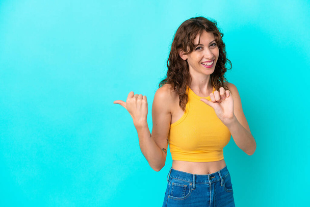 Young woman with curly hair isolated on blue background pointing to the side to present a product - Photo, image