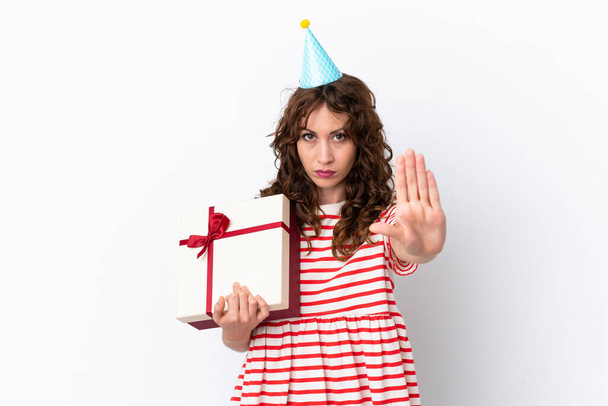 Young woman with curly hair holding present isolated on white background making stop gesture - Фото, изображение