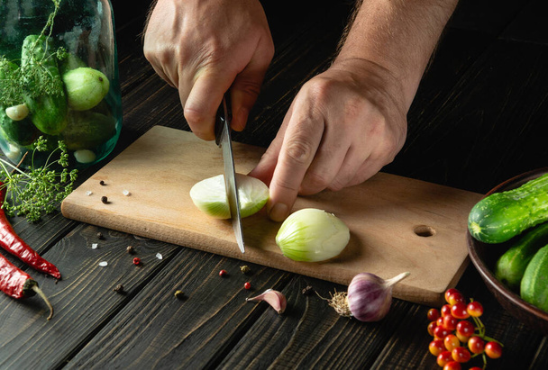 The chef cuts fresh onions for pickling or pickling with spices and cucumbers in a jar. Close-up of a cook hands while working on a kitchen table - 写真・画像