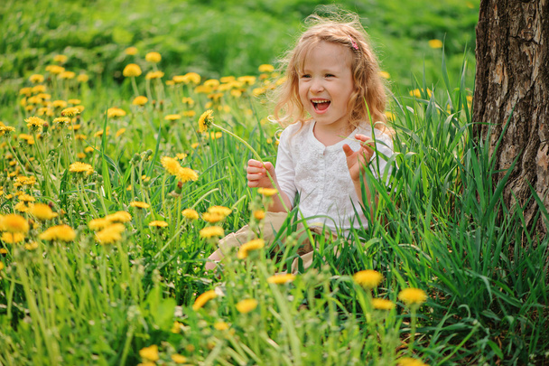 Cute blonde child girl having fun on spring dangelion field - Foto, afbeelding