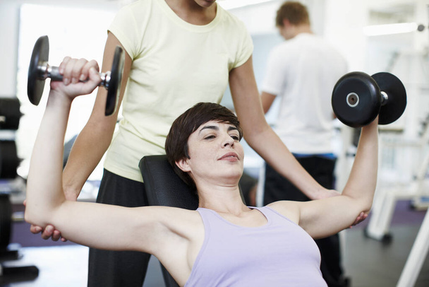 Hilfe bei ihrer Form. eine attraktive junge Frau, die mit ihrem Personal Trainer Gewichte trainiert - Foto, Bild