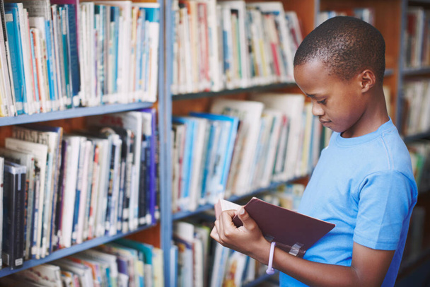 Les bibliothèques sont un endroit idéal pour les esprits créatifs. Un garçon afro-américain profitant d'un bon livre à la bibliothèque - Photo, image
