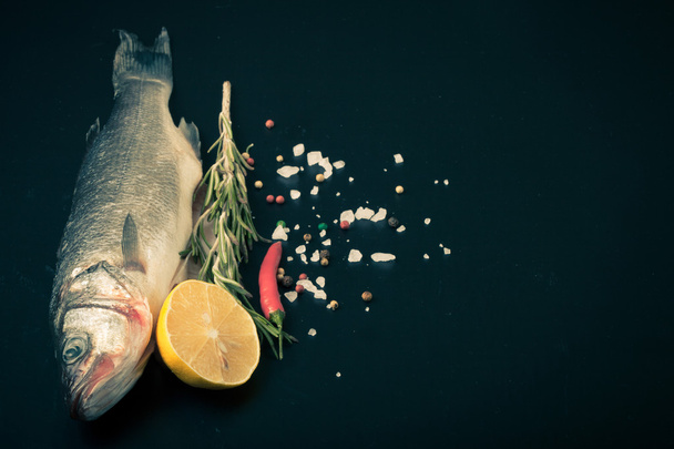 Fresh sea fish lying on dark background with spices. Space for t - Fotó, kép
