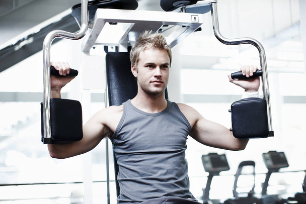 Focused on his workout. a handsome young man using an exercise machine in the gym - Foto, Imagem