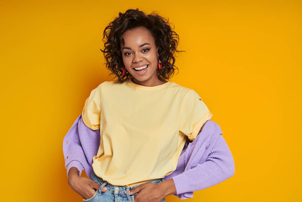 Attractive African woman looking at camera and smiling while standing against yellow background - Foto, Bild