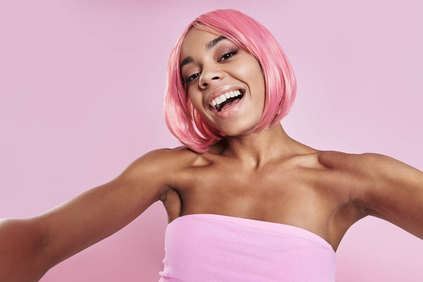 Щаслива африканка з рожевим волоссям робить селфі проти рожевого фону. - Фото, зображення