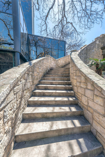 Escadaria ao ar livre com degraus de concreto iluminado pelo sol e grades de pedra em um dia ensolarado. Vista a partir do fundo de uma escada do parque com edifício de vidro e fundo azul céu. - Foto, Imagem