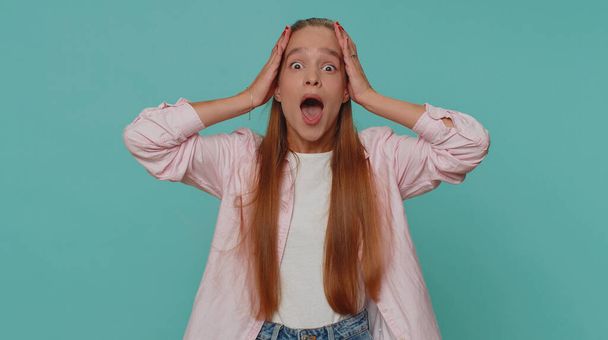 Oh my God, Wow. Excited amazed girl looking surprised at camera with big eyes, shocked by sudden victory game winning, lottery goal achievemen, good news. Child kid on blue studio background indoor - Foto, Imagen