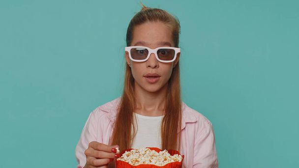 Excited teenager girl eating popcorn and watching interesting tv serial, sport game film, online social media movie content online. Student child kid on blue background enjoying domestic entertainment - Foto, Imagem