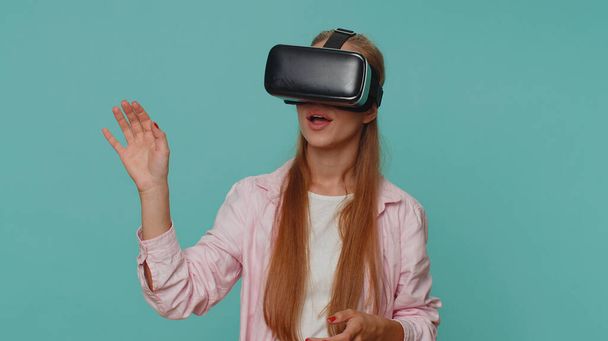 Excited teenager young girl using headset helmet app to play simulation game. Watching virtual reality 3D 360 video. Student child kid in VR goggles device isolated on blue studio background indoors - Photo, image