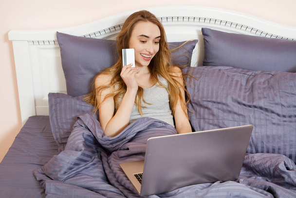 Жінка використовує ноутбук для покупки онлайн в ліжку вдома, оплата кредитною карткою з онлайн-банкінгом транзакцій. Щаслива дівчина вказала на кредитну картку
. - Фото, зображення