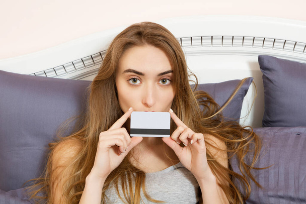 Красива жінка з кредитною карткою на ліжку в її спальні
 - Фото, зображення