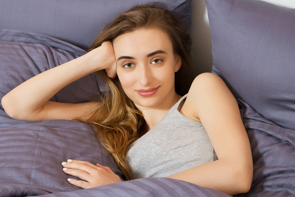 Woman lying on her bed looking at the camera with a smile - Photo, Image