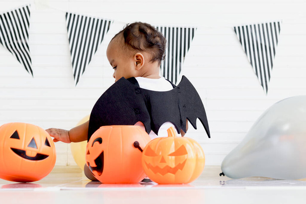Back of adorable African baby kid dressing up in vampire fancy Halloween costume with black bat wings, cheerful little cute child go to party, playing trick or treat, Happy Halloween celebration. - Fotó, kép