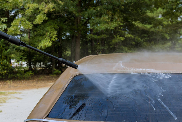 Je tu muž, který si myje auto pod vysokotlakým tryskovým postřikem vodou čisticím prostředkem. - Fotografie, Obrázek