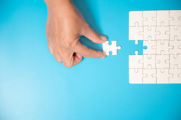 Nahaufnahme Hand halten und spielen Puzzle-Spiel unvollständig. Weiße Puzzleteile auf blauem Hintergrund. Konzepte der Problemlösung, des Business, der Teamarbeit. - Foto, Bild