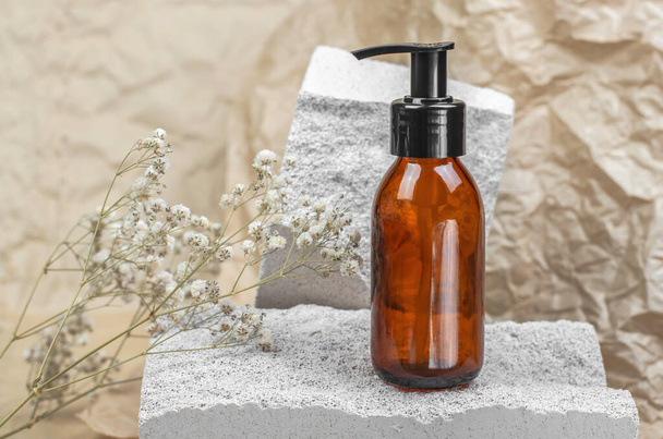 Brown cosmetic bottle with a pump on a white natural stone podium. Body care - Фото, зображення