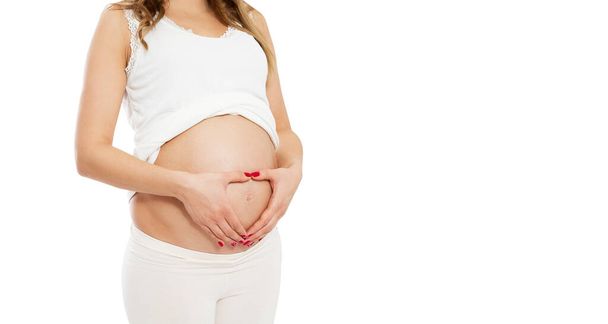 Έγκυος γυναίκα κάνει σχήμα καρδιάς με τα χέρια στην κοιλιά - περικοπή εικόνας. - Φωτογραφία, εικόνα