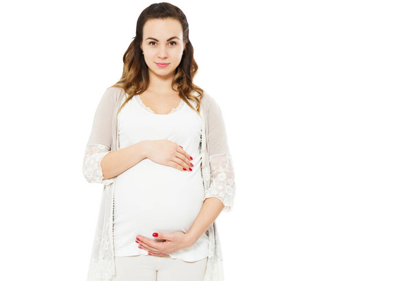 Pretty young pregnant woman standing on white background and touches the pregnant belly. - Fotó, kép