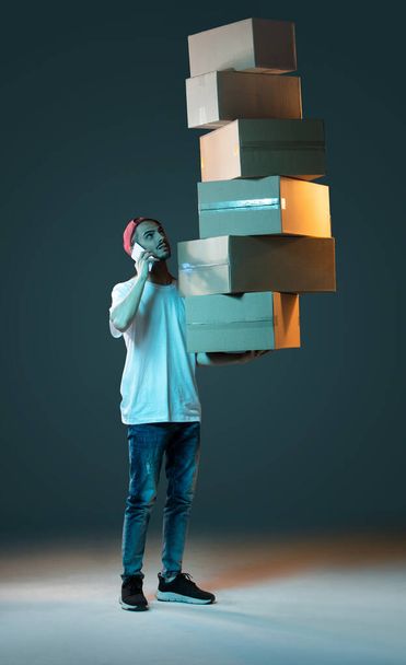 Emotional delivery guy with a lot of boxes on a dark blue background - 写真・画像