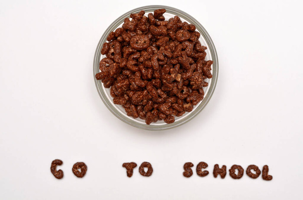 шоколадные хлопья в миске и текст идти в школу из букв алфавита на белом фоне - Фото, изображение