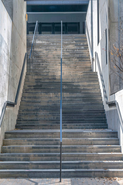 Escalera de un edificio que conduce a la planta superior y puerta de entrada de cristal. Vista desde la parte inferior de una escalera con barandillas de acero y escalones de hormigón en un día soleado en Austin Texas. - Foto, imagen