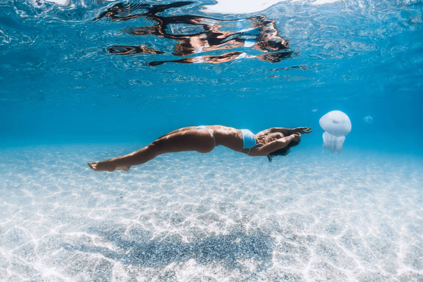 Woman glides over sandy bottom underwater. Young lady posing with jelly fish in blue ocean - Photo, Image