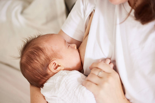 Mother breastfeeding her newborn baby boy. Realistic home portrait - Zdjęcie, obraz