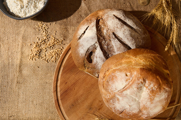 Első látásra. Friss, házi készítésű kenyérből készült kenyér egy fapadlón, szétszórt gabonával és búzapecsenyével egy vászonterítőn. Csendélet egészséges pékséggel, dúsított élelmi rostokkal. Reklámhely másolása - Fotó, kép